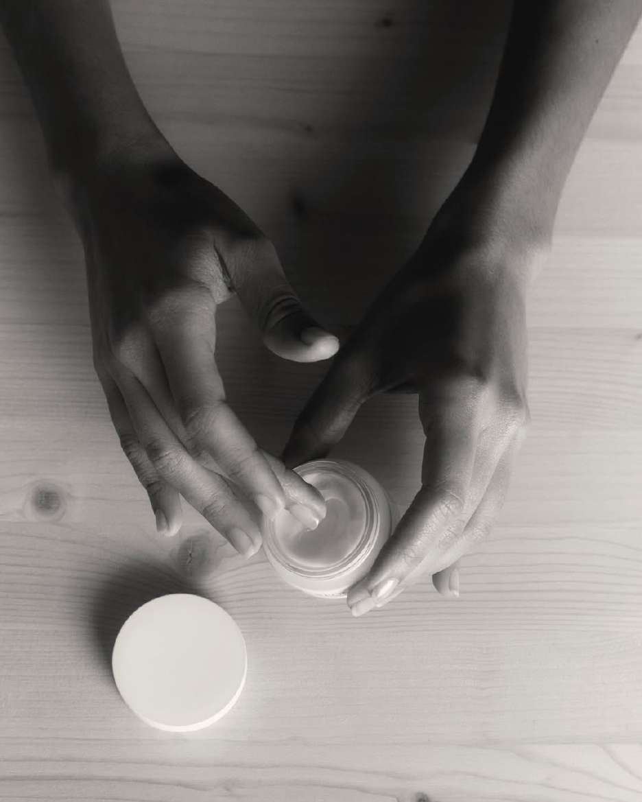 Hands opening a jar of cream on a pale wooden table
