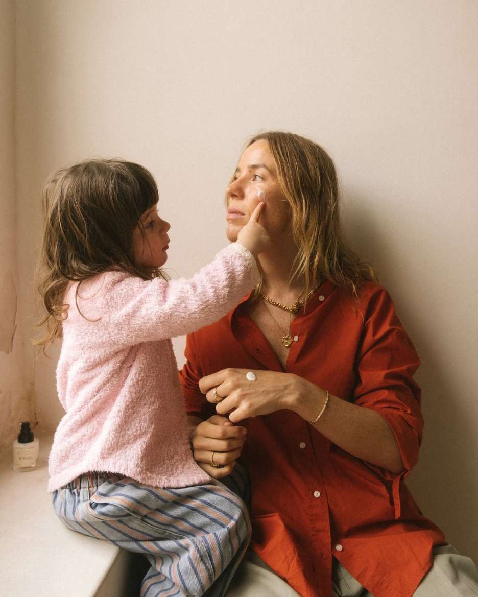 A child applying cream to her mother's cheek